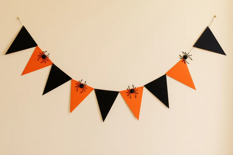 Halloween paper bunting with alternating orange and black triangles and spiders hanging on a wall