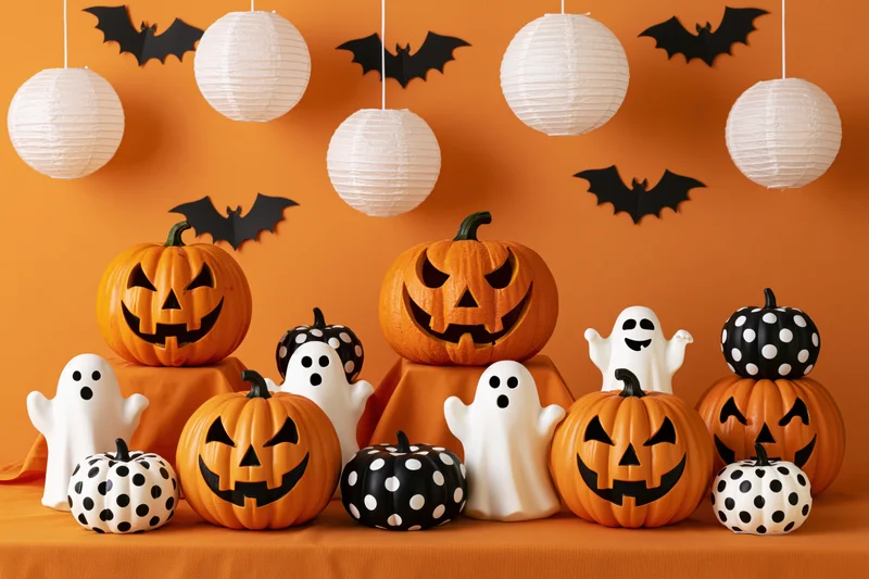 Carved pumpkins and ghost figures arranged on a table with hanging paper lanterns and bats against an orange backdrop