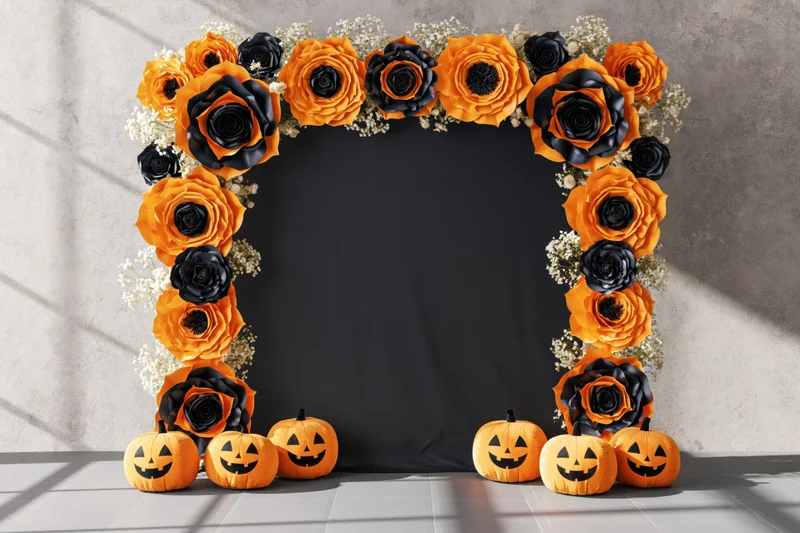 Halloween photo booth backdrop with orange and black paper roses and jack-o-lanterns arranged in an arch frame against a concrete wall