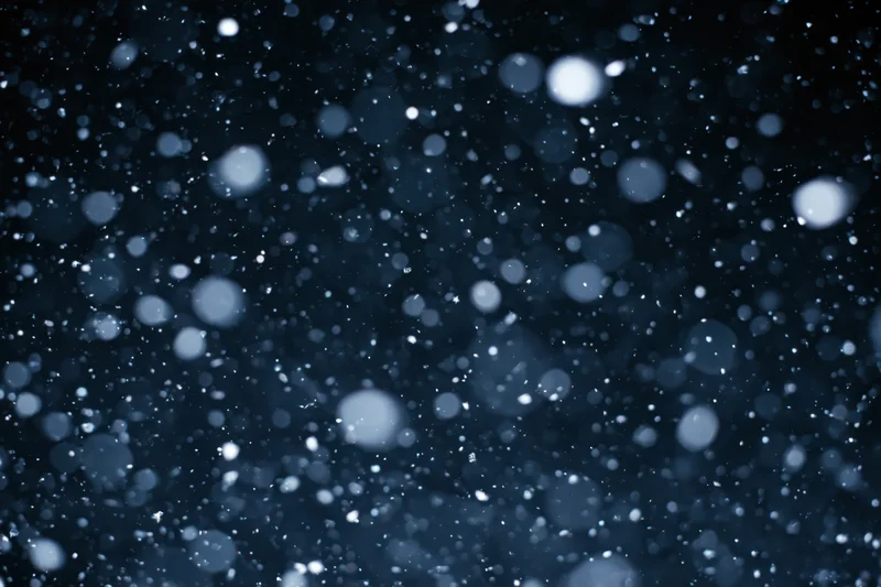 Snowflakes falling midair against dark night sky
