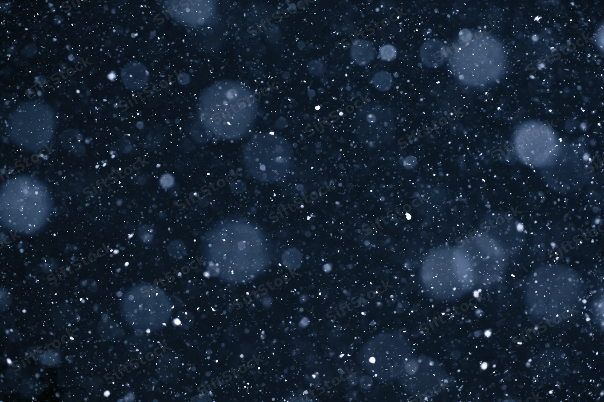 Snow falling against a dark night sky with bokeh highlights