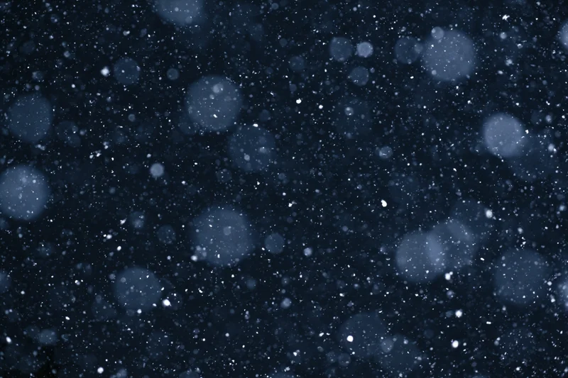Snow falling against a dark night sky with bokeh highlights
