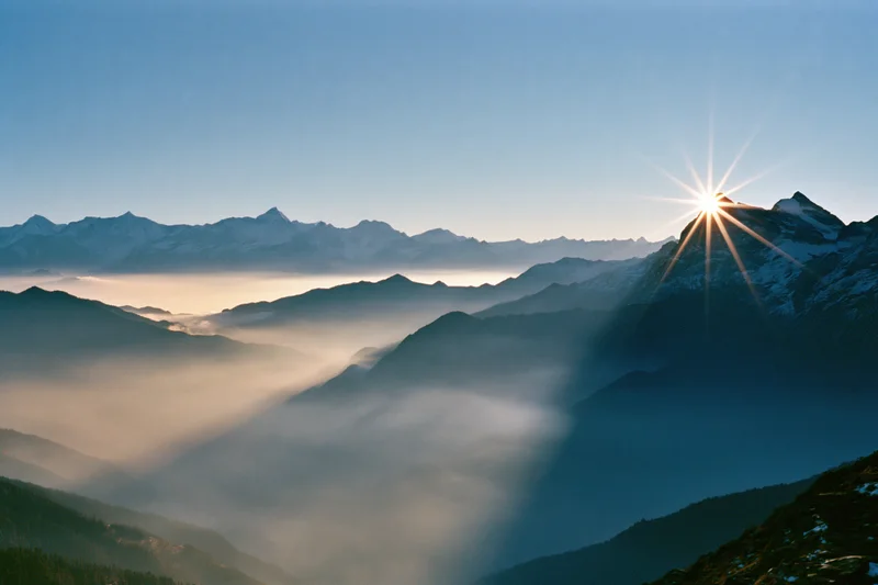 Snow-capped mountain peaks rising above a sea of fog at sunrise