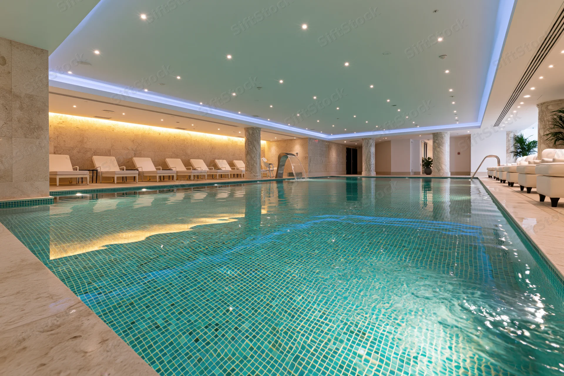 Indoor spa pool with mosaic tiles and lounge chairs in a luxury hotel setting