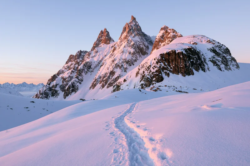 Snow-covered mountain peaks with footprints leading across a snowy slope at sunrise