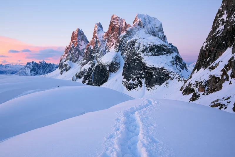 Snow-covered mountain peaks with footprints in the foreground at dawn