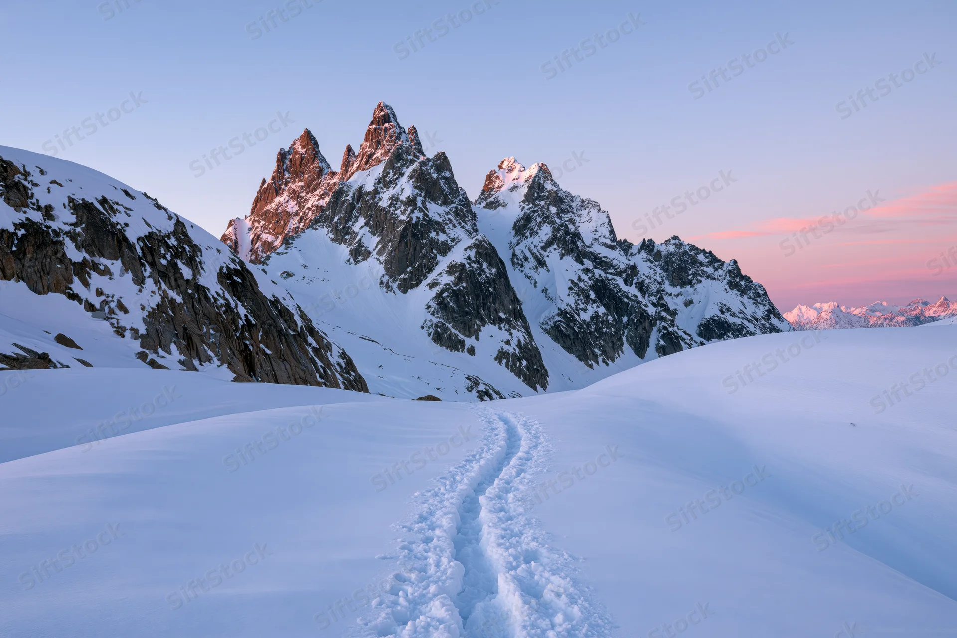 Snow-covered mountain peaks with footprints leading toward jagged summits in alpine winter landscape