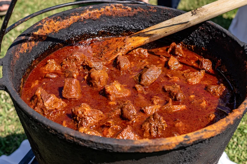 Deep red meat stew simmering in a blackened cast iron cauldron outdoors