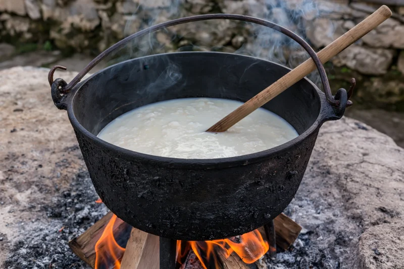 Blackened cast iron cauldron simmering over open fire outdoors