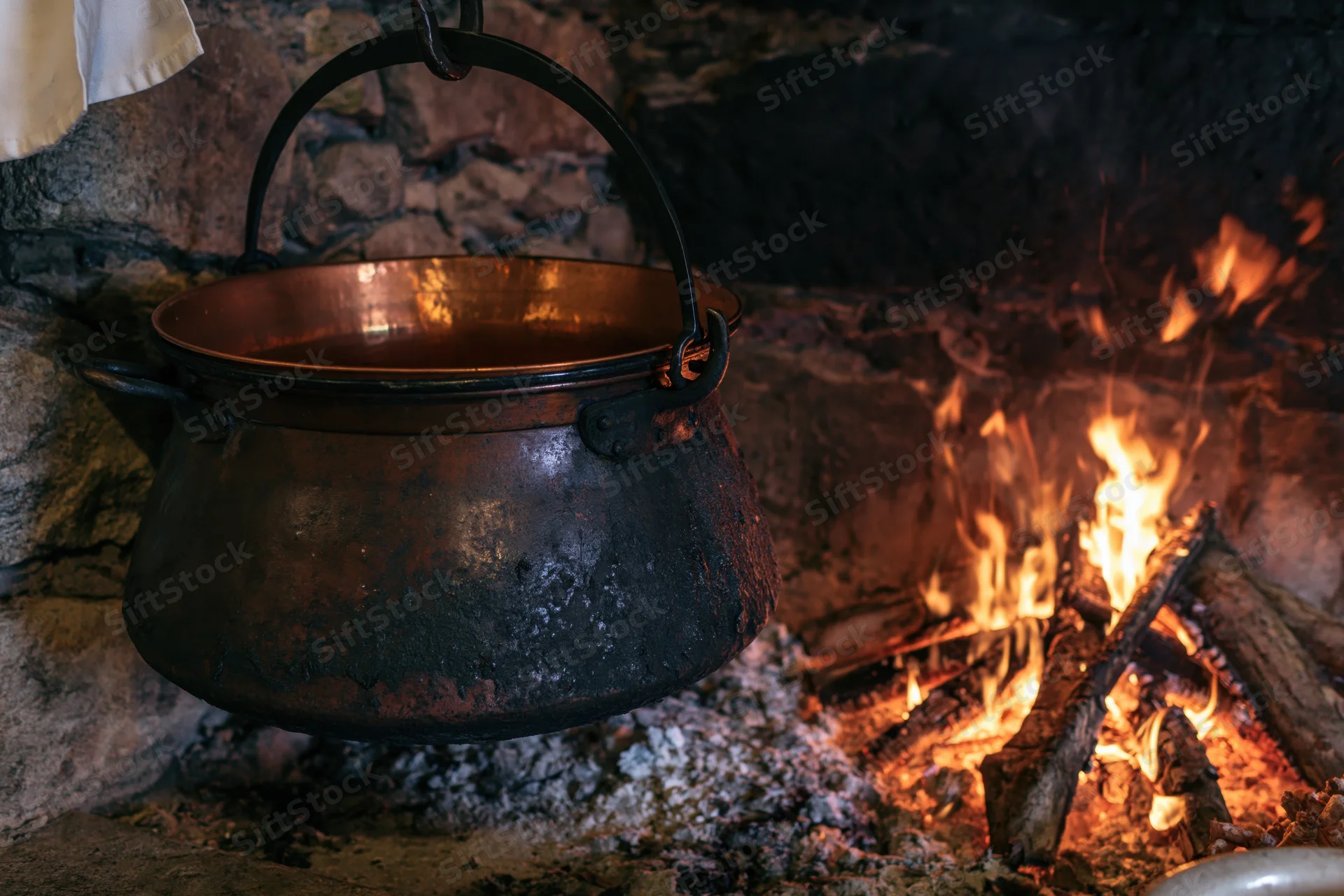 Blackened copper cauldron hanging over open fire in stone fireplace