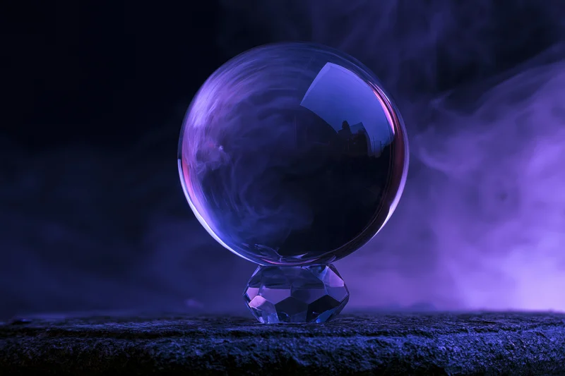 Crystal ball resting on a faceted base with purple smoke swirling around it on a dark textured surface