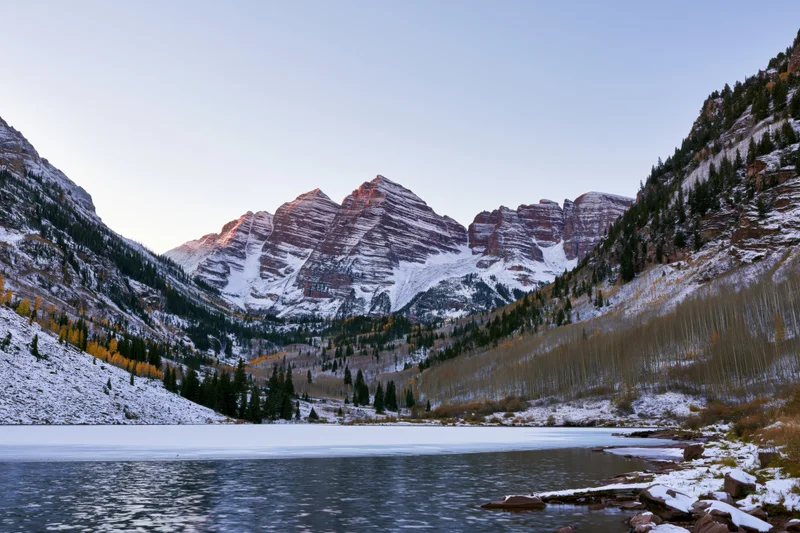 Snow-covered maroon bells peaks rising above a frozen lake in a mountain valley at twilight