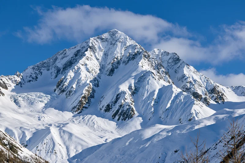 Snow-covered mountain peak rising against a clear blue sky with scattered clouds