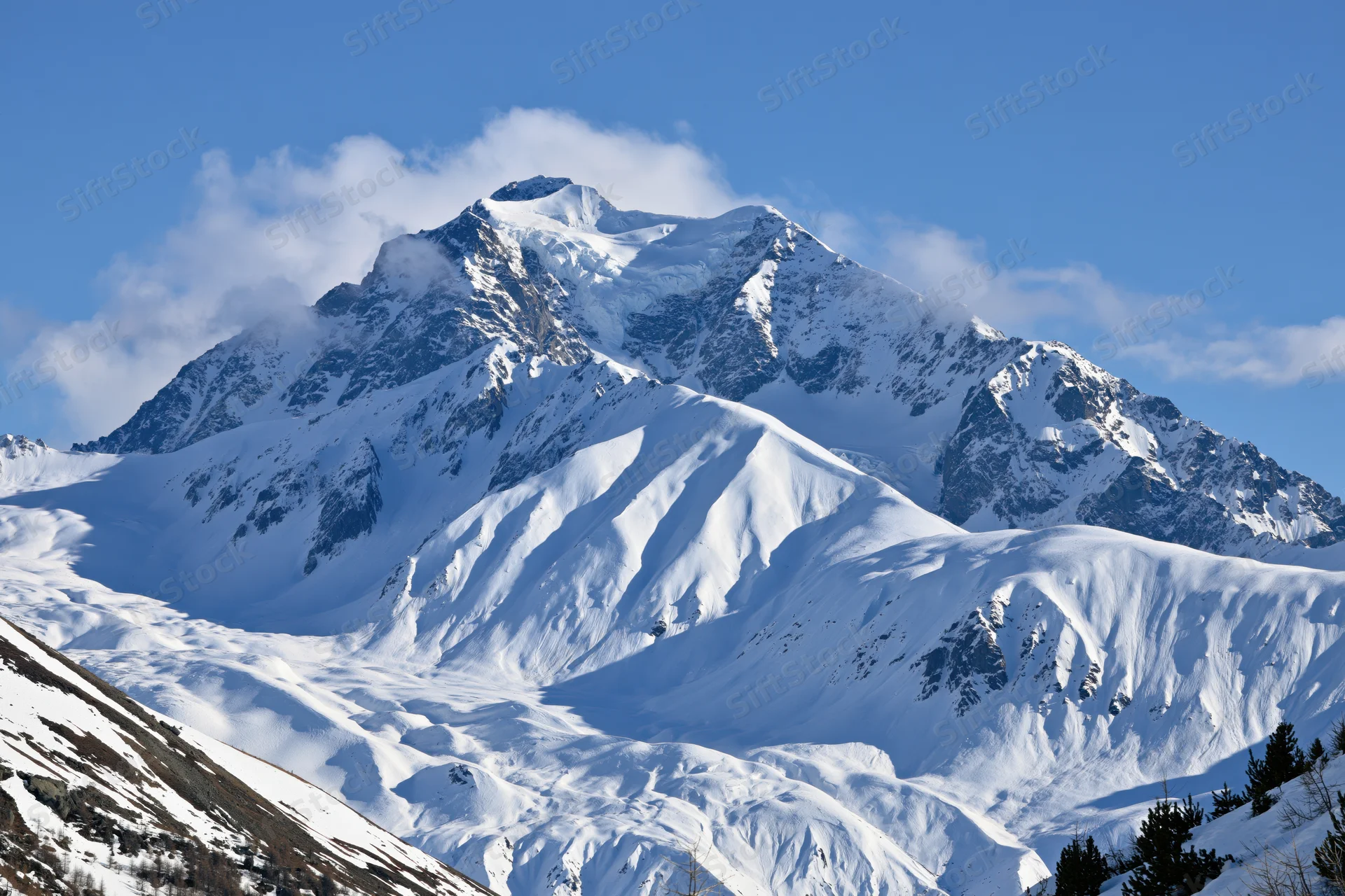 Snow-covered mountain peak rising against a clear blue sky with clouds drifting around its summit
