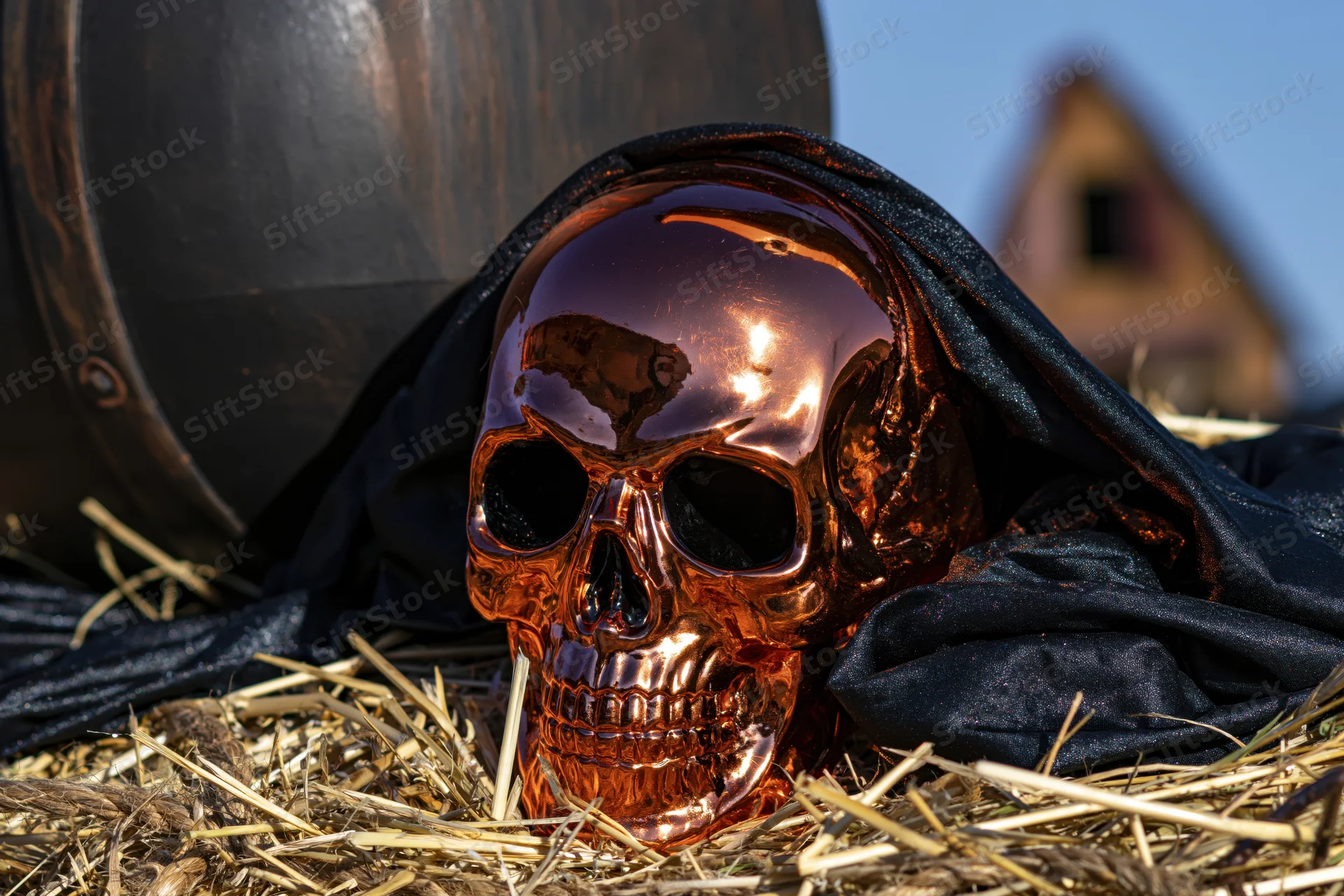Copper metallic skull resting on hay beside a barrel under a clear sky