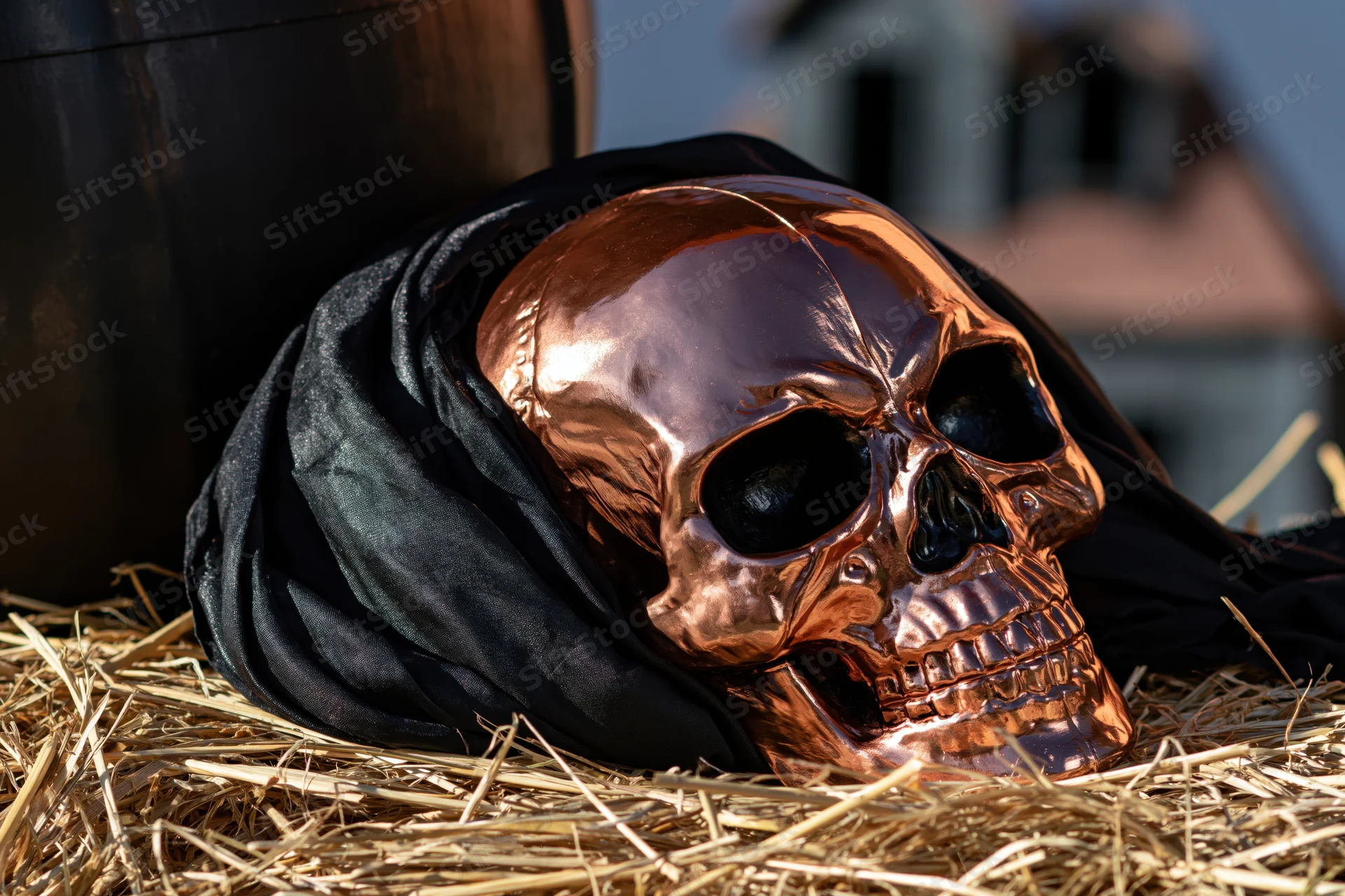 Copper skull wrapped in black cloth resting on hay near a barrel outdoors