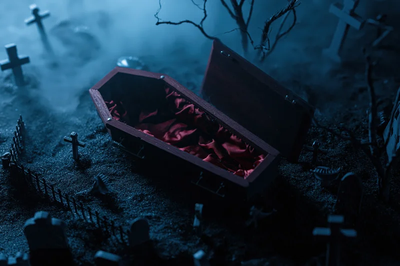 Open wooden coffin with red satin interior in miniature graveyard scene at night