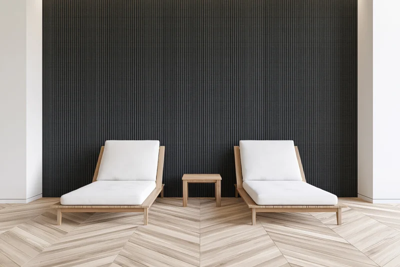Two white lounge chairs with wooden frames arranged symmetrically in a minimalist spa relaxation room with black textured wall and herringbone wood flooring