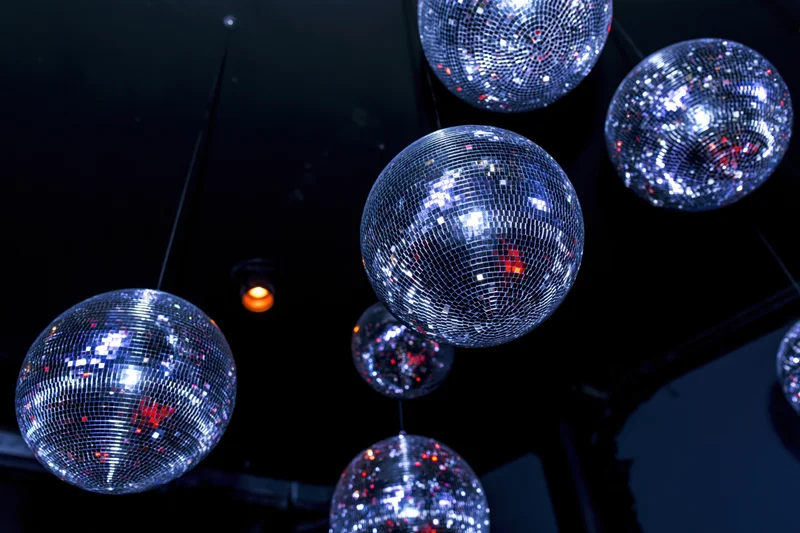 Multiple mirror disco balls hanging from ceiling reflecting colorful lights in dark club interior