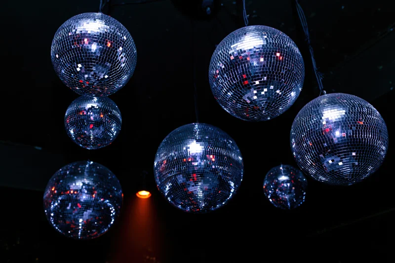 Multiple mirror disco balls of varying sizes hanging from ceiling reflecting colorful lights in dark venue