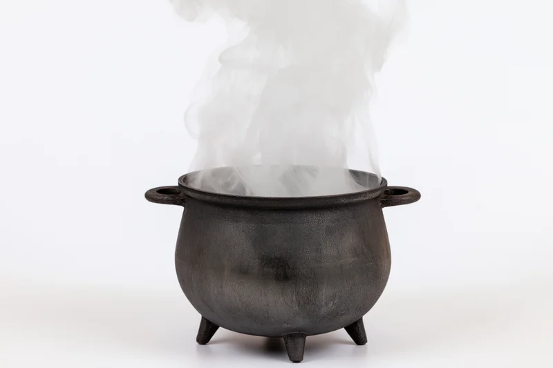 Black cast iron cauldron steaming with white smoke on white background