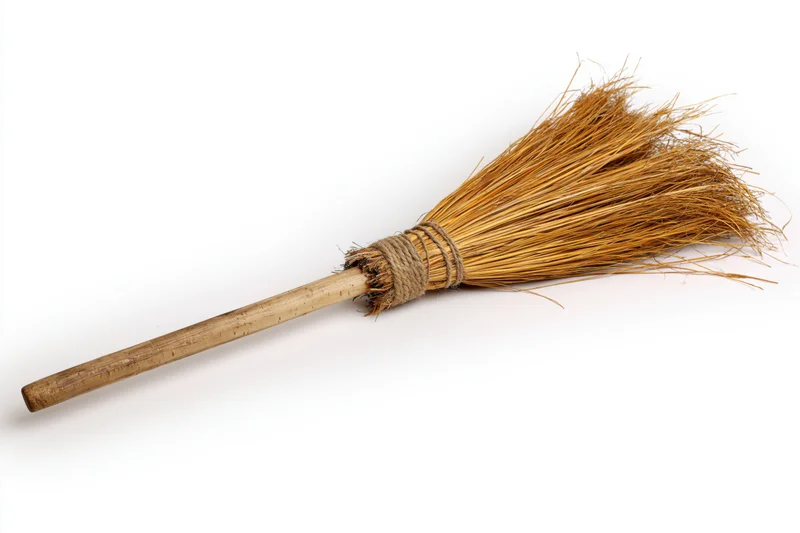 Old handmade straw broom with wooden handle lying diagonally on white background