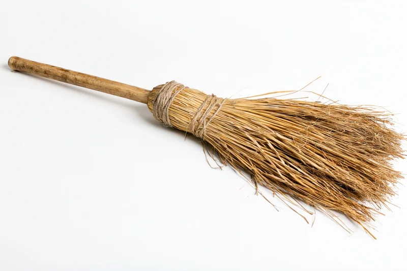 Old handmade straw broom with wooden handle lying diagonally on white background