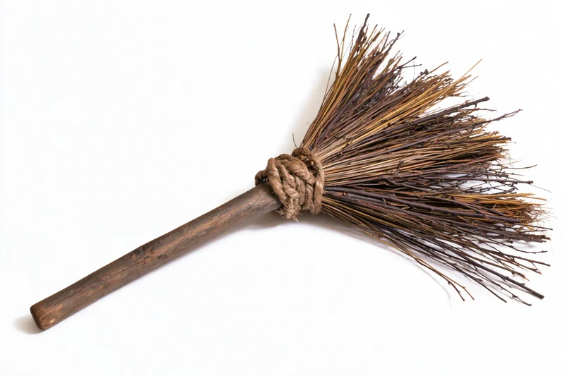 Old handmade twig broom with wooden handle and rope binding lying diagonally on white background