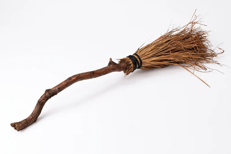 Old handmade witch broom with gnarled wooden handle and straw bristles on white background