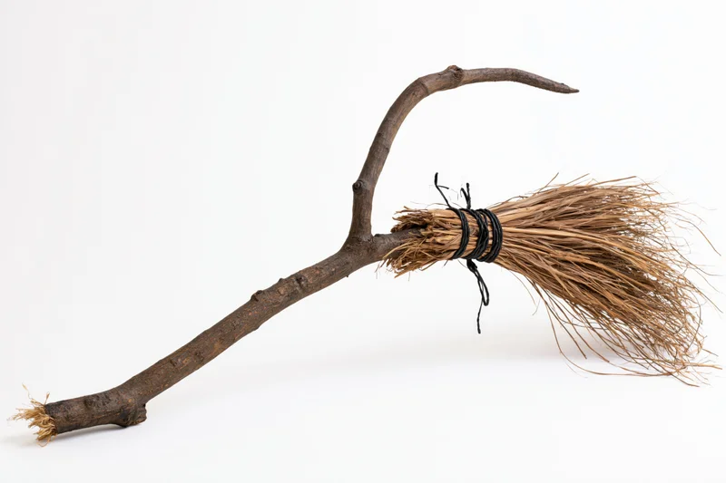 Handmade witch broom with curved wooden handle and straw bristles on white background