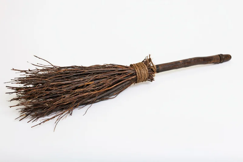 Old handmade witch's broom lying horizontally on white background