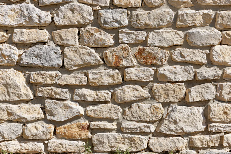 Close-up of an old rustic stone wall with uneven natural stones and mortar joints under sunlight