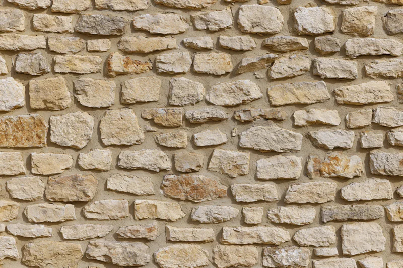 Old rustic stone wall with irregular natural stones and mortar filling the frame