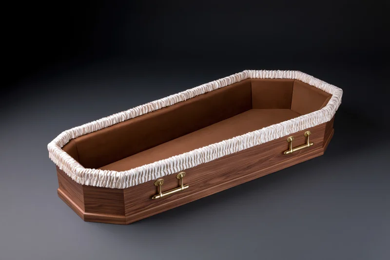 Open empty wooden coffin with white ruffled lining and brass handles viewed from above at slight angle on dark gradient background