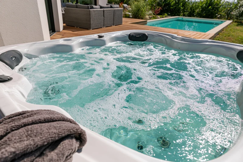 Bubbling turquoise water in an outdoor hot tub on a sunny backyard deck near a swimming pool