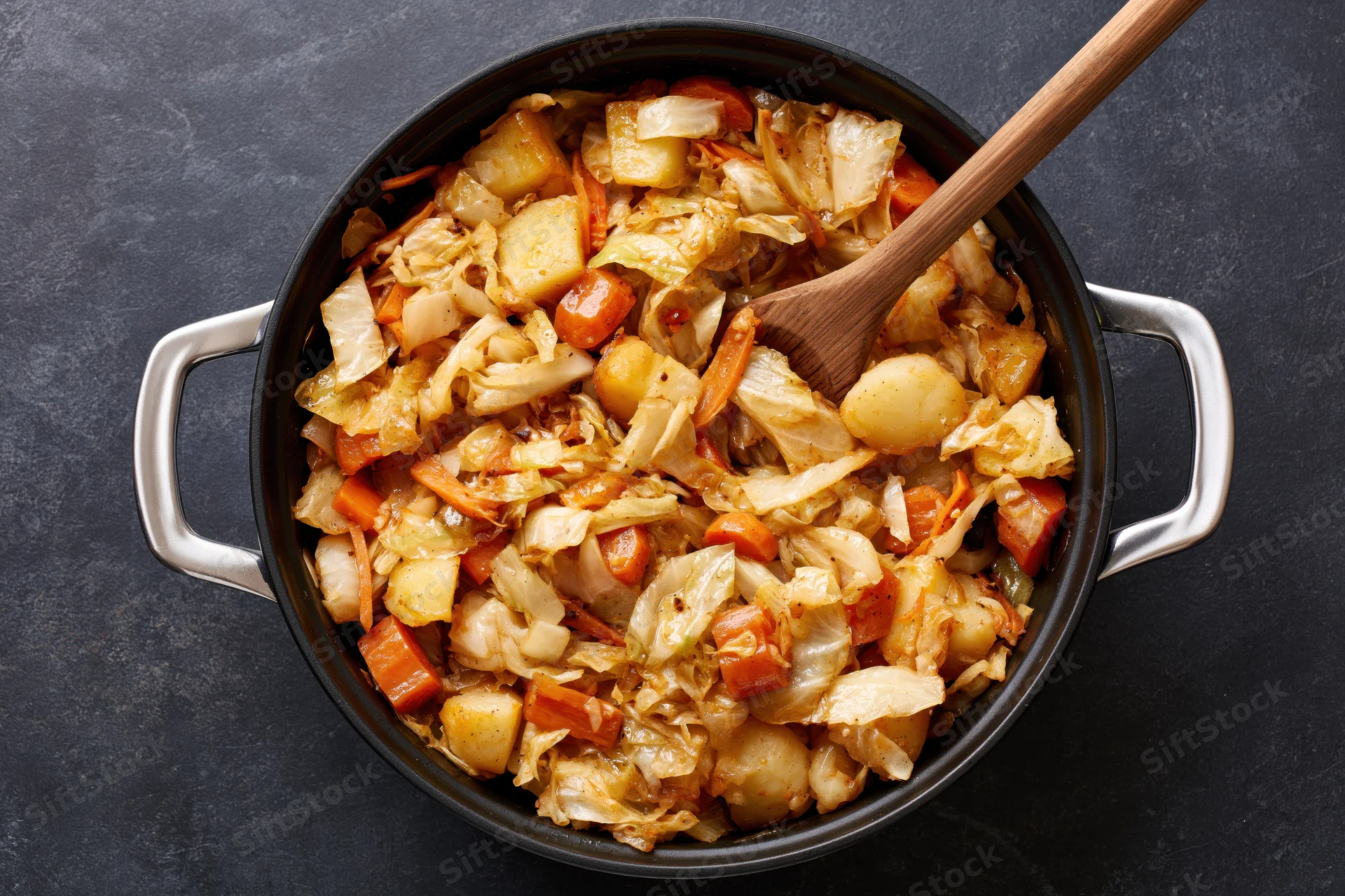 Sauteed cabbage and vegetables in a black cast iron pot with wooden spoon overhead view
