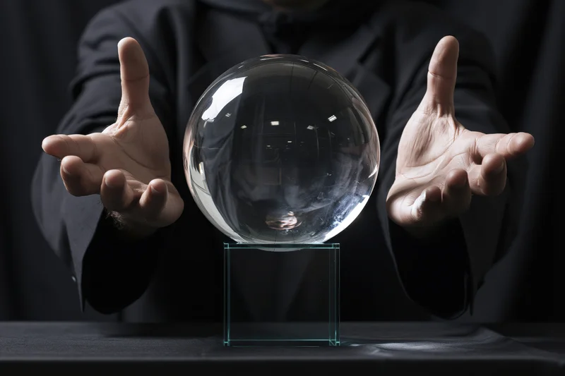 Magician hovering hands around a crystal ball on a stand at a table