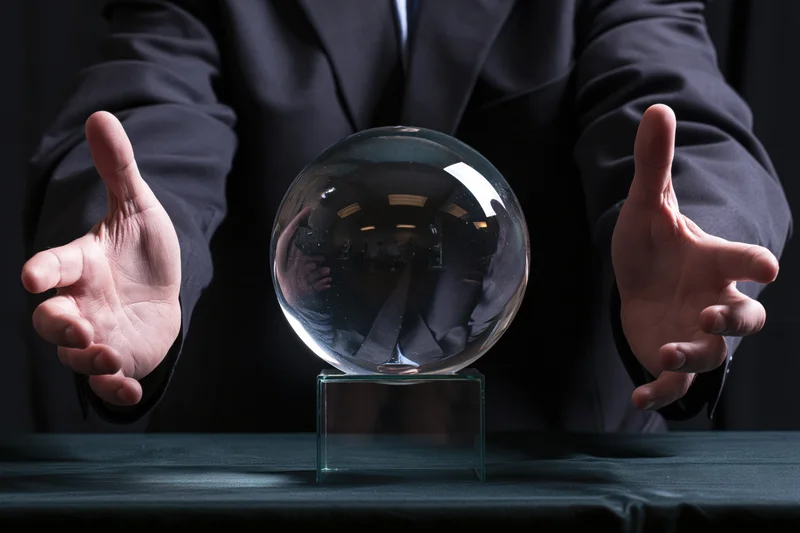 Magician in dark suit with open hands framing a crystal ball on a table