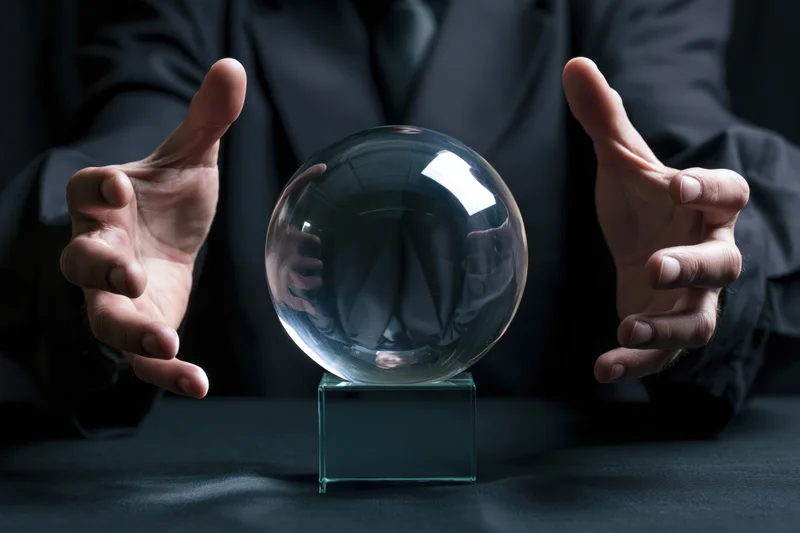 Man in dark suit hovering hands around crystal ball on table