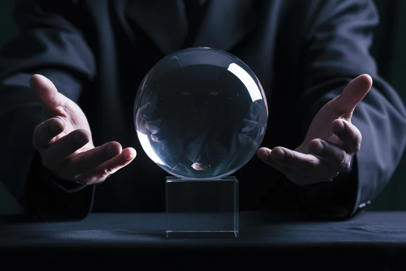 Man in dark suit hovering hands around crystal ball on table