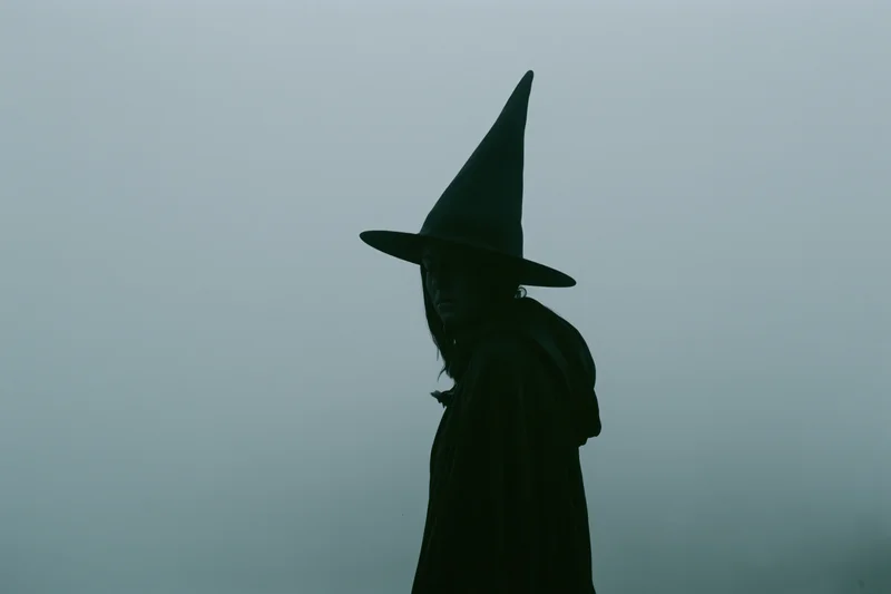 Silhouette of a woman in a pointed witch hat and dark cloak standing in fog