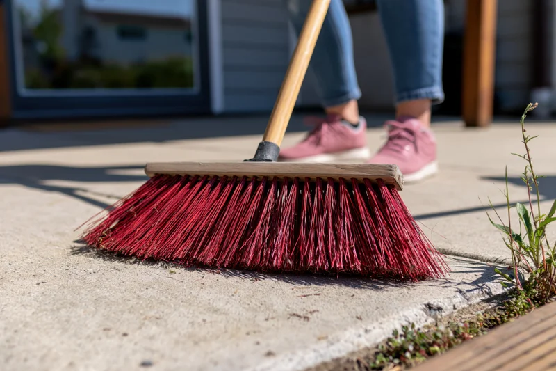 Woman sweeping concrete patio with red-bristled broom outdoors