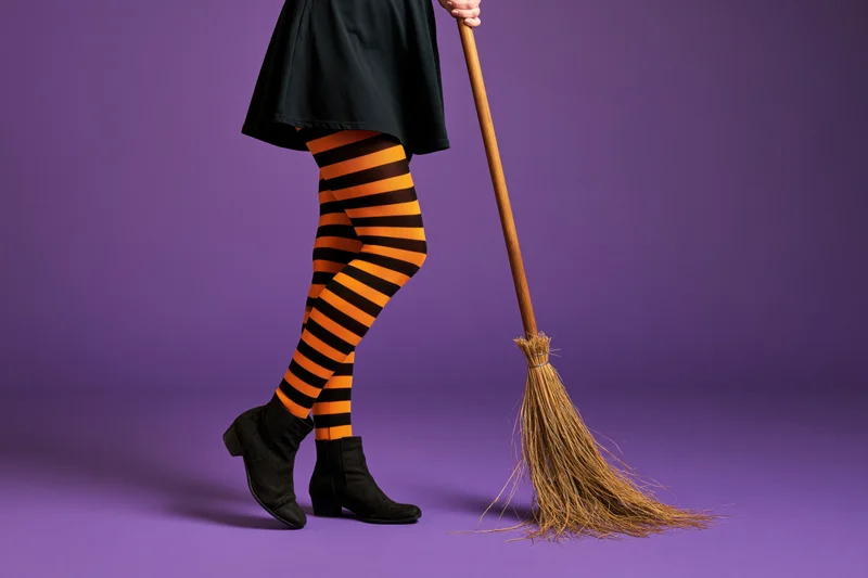Woman in witch costume holding broom against purple background