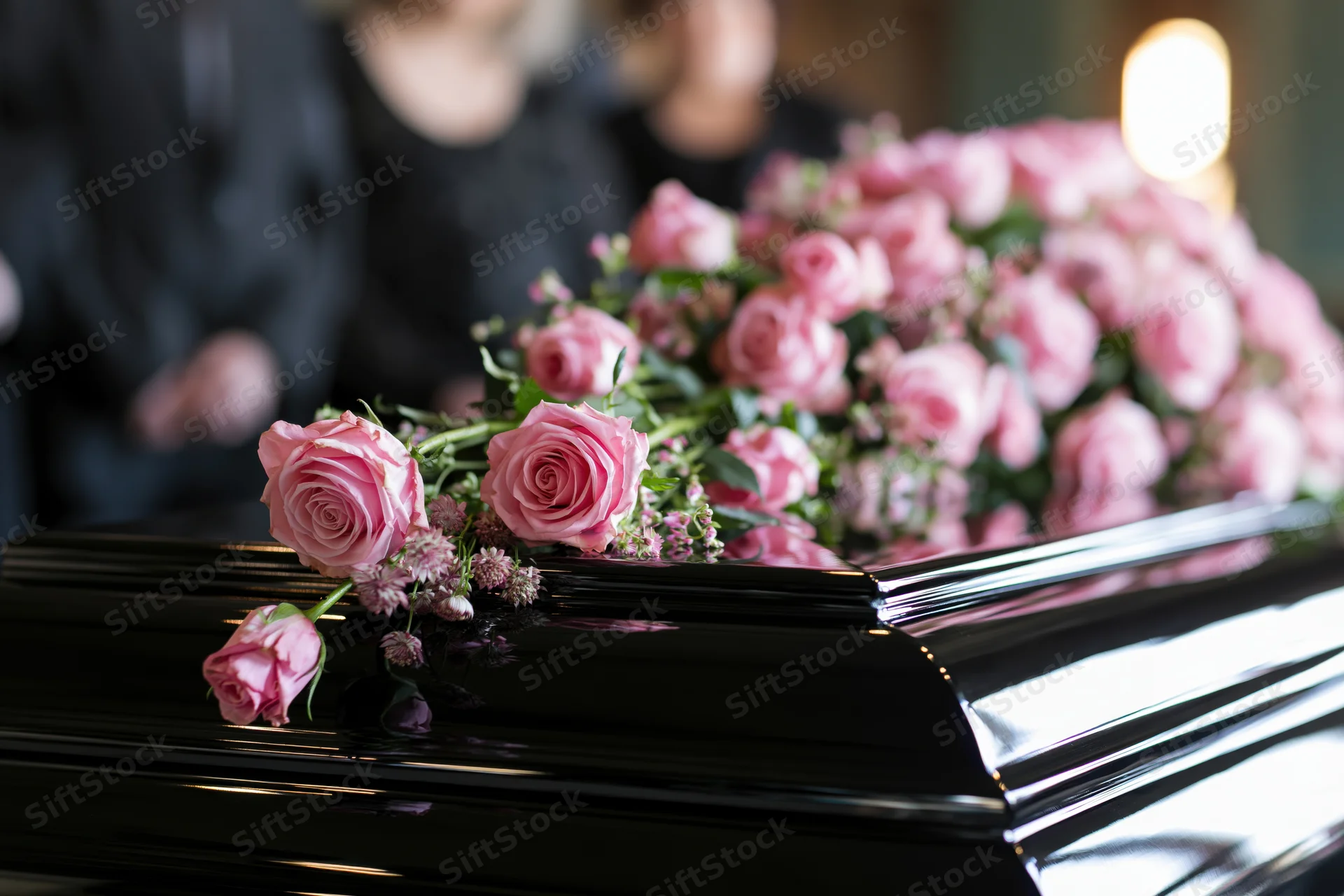 Pink roses and small flowers arranged on a black polished coffin at a funeral service