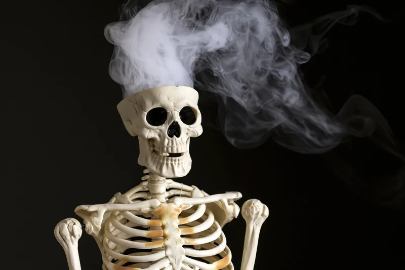 Plastic human skeleton model with smoke rising from its skull against black background