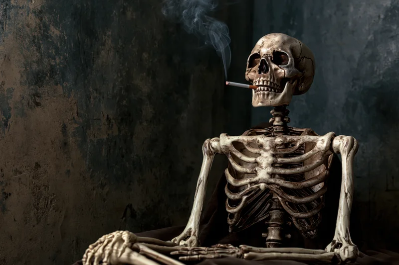 Human skeleton prop smoking a cigarette against a dark textured wall