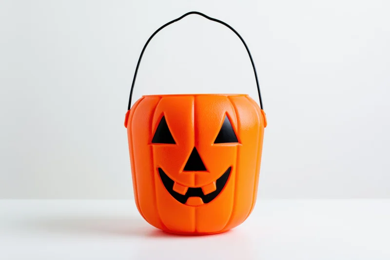 Orange plastic jack-o-lantern bucket with black face design on white surface