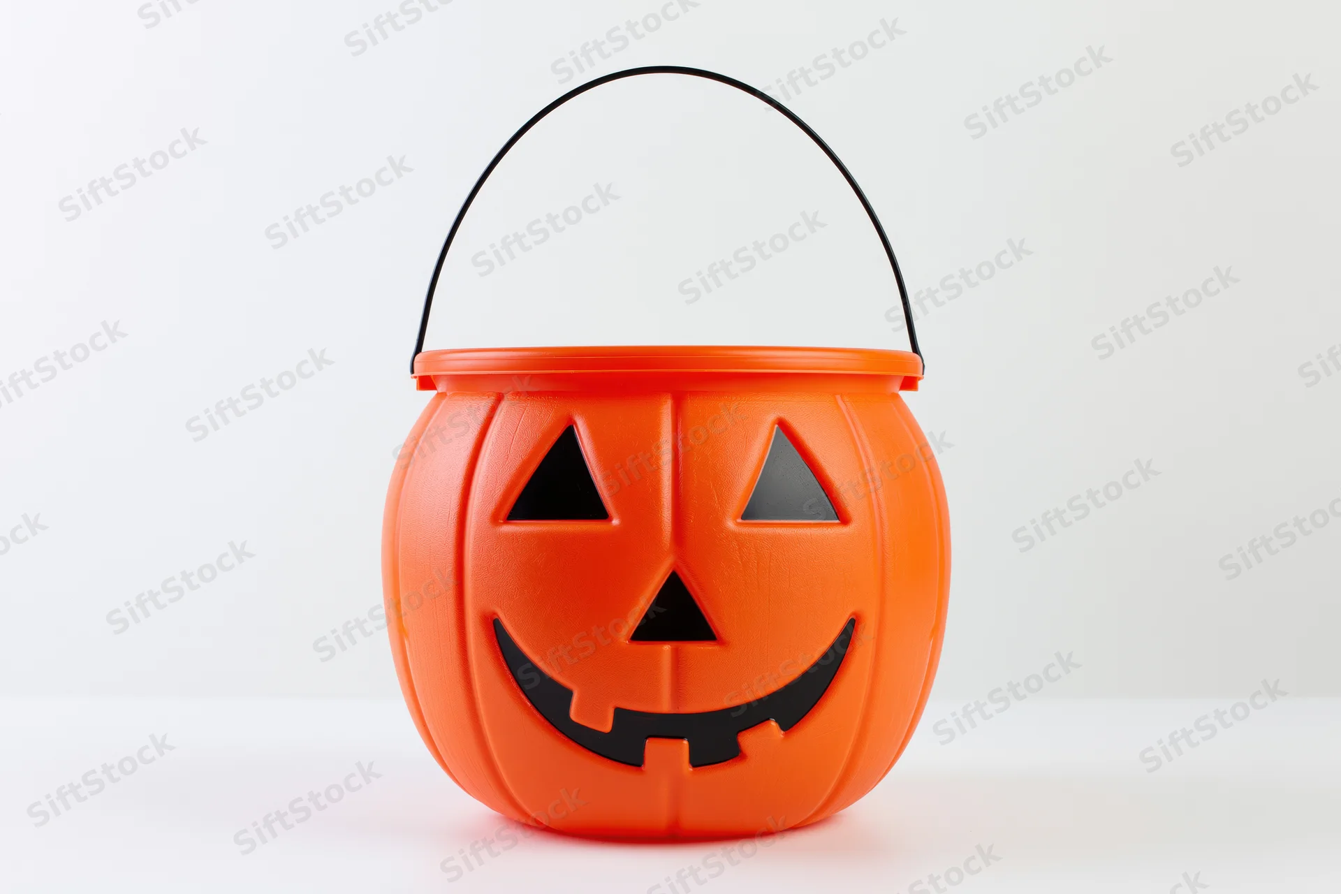 Orange plastic jack-o-lantern bucket with smiling face and black handle on white background