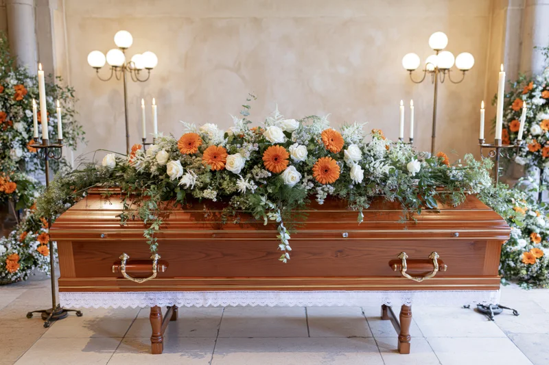 Polished wooden coffin adorned with orange and white floral arrangement in a chapel setting
