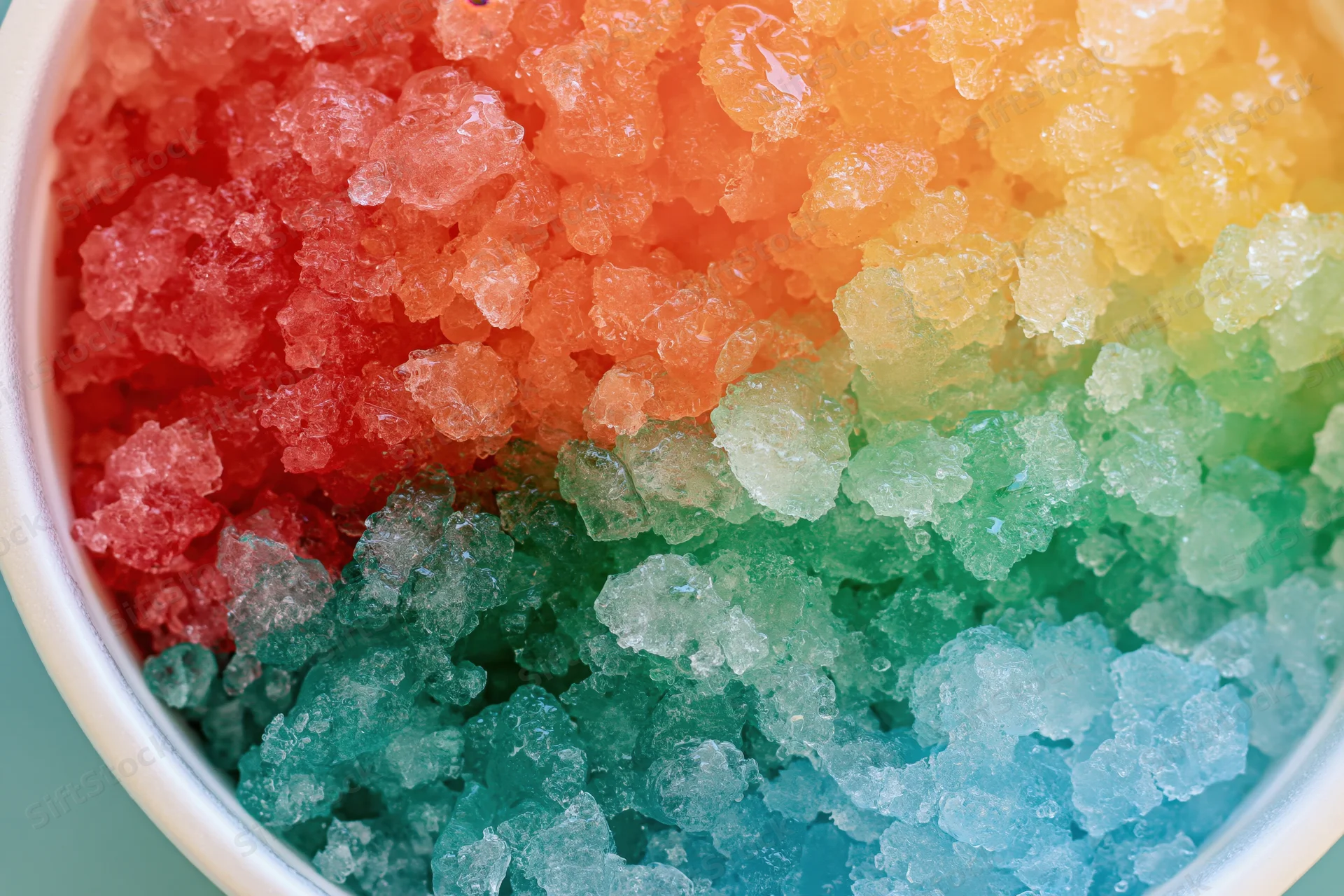 Rainbow shave ice in a white cup viewed from directly overhead